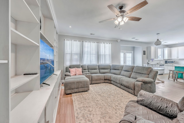 living room with light hardwood / wood-style floors, ornamental molding, and ceiling fan