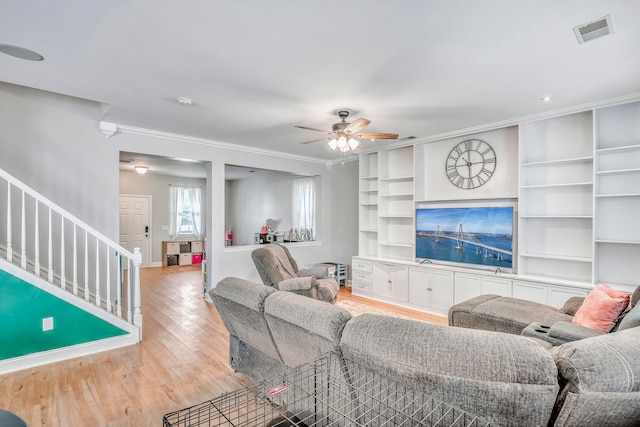 living room featuring ceiling fan, light wood-type flooring, crown molding, and built in shelves