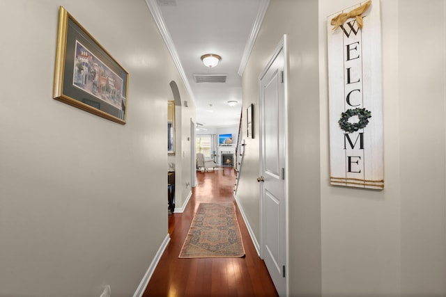 hall featuring visible vents, baseboards, arched walkways, ornamental molding, and dark wood-type flooring