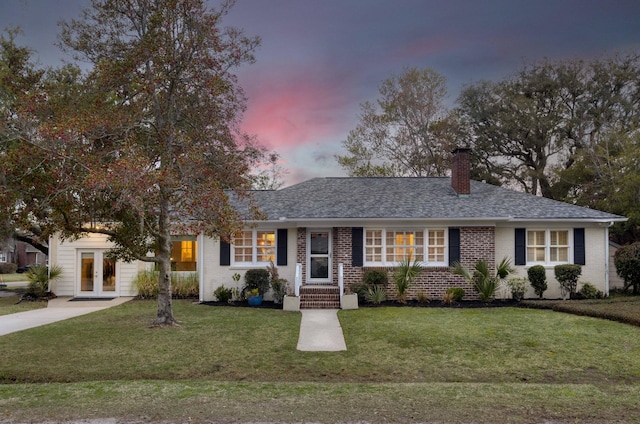 single story home with brick siding, a chimney, a front yard, and a shingled roof