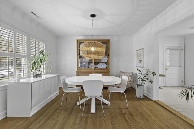 dining room featuring wood finished floors, visible vents, baseboards, an inviting chandelier, and crown molding