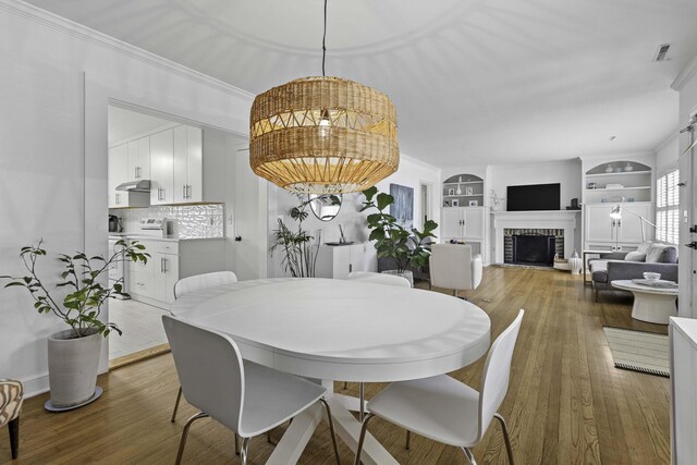 dining room with visible vents, built in shelves, ornamental molding, wood-type flooring, and a brick fireplace