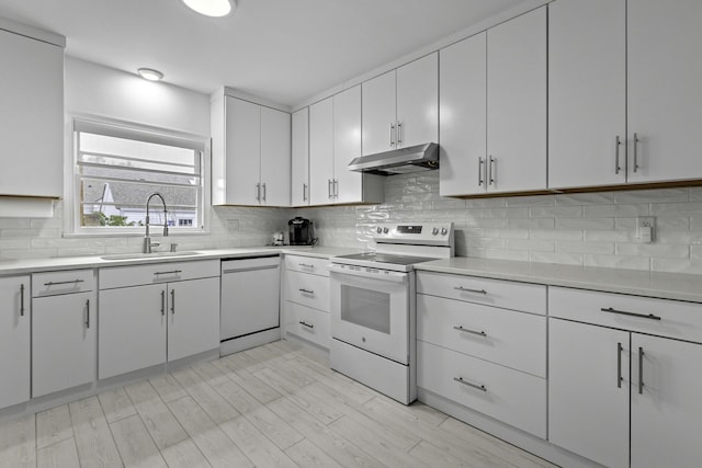 kitchen with decorative backsplash, white appliances, under cabinet range hood, and a sink