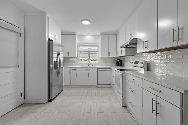 kitchen with a sink, under cabinet range hood, backsplash, white appliances, and light wood-style floors