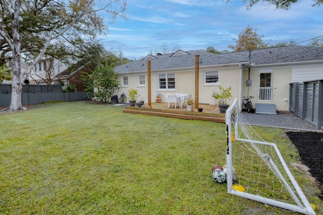 rear view of house featuring fence, a yard, a shingled roof, a deck, and brick siding