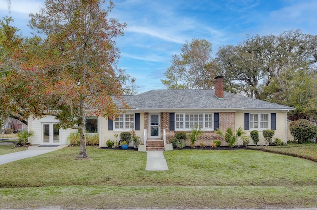 ranch-style house featuring a front yard, a shingled roof, a chimney, french doors, and brick siding