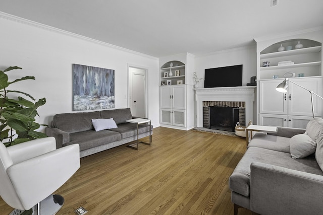 living area with built in features, a brick fireplace, crown molding, and wood finished floors