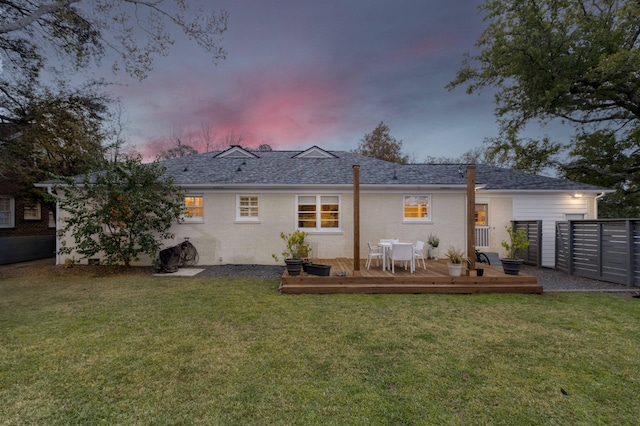 back of house at dusk featuring brick siding, a wooden deck, a yard, and fence