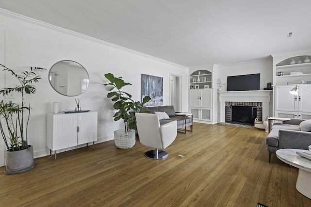 living area featuring baseboards, built in features, ornamental molding, a fireplace, and hardwood / wood-style flooring