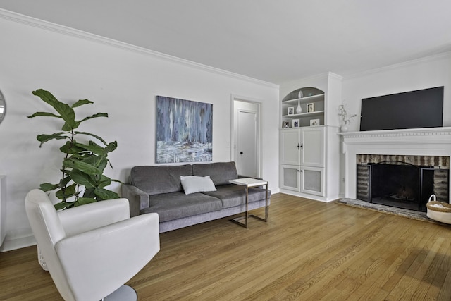 living room featuring built in features, a brick fireplace, wood finished floors, and ornamental molding