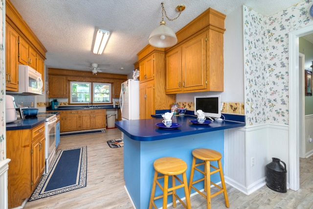 kitchen featuring a textured ceiling, white appliances, light hardwood / wood-style flooring, and a breakfast bar