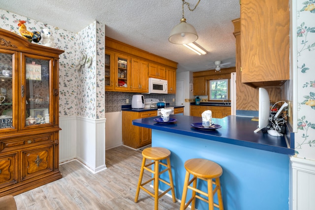 kitchen with a textured ceiling, white appliances, light hardwood / wood-style flooring, hanging light fixtures, and kitchen peninsula