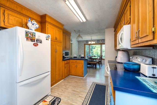 kitchen with light wood-type flooring, a notable chandelier, white appliances, a textured ceiling, and kitchen peninsula