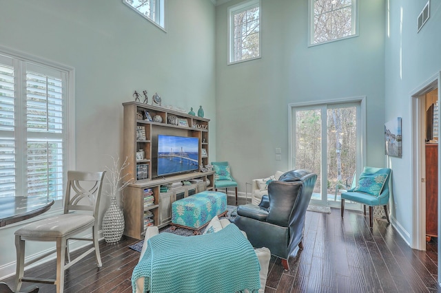 living area featuring a towering ceiling, dark wood-style floors, baseboards, and visible vents