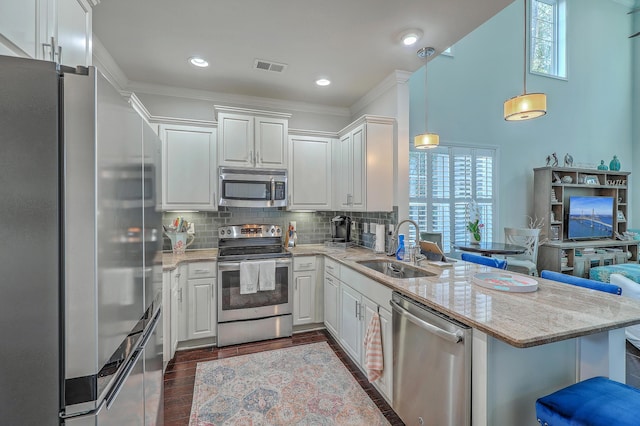 kitchen featuring stainless steel appliances, a peninsula, a sink, white cabinets, and tasteful backsplash