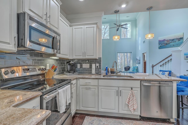 kitchen with stainless steel appliances, decorative backsplash, white cabinetry, a sink, and a peninsula