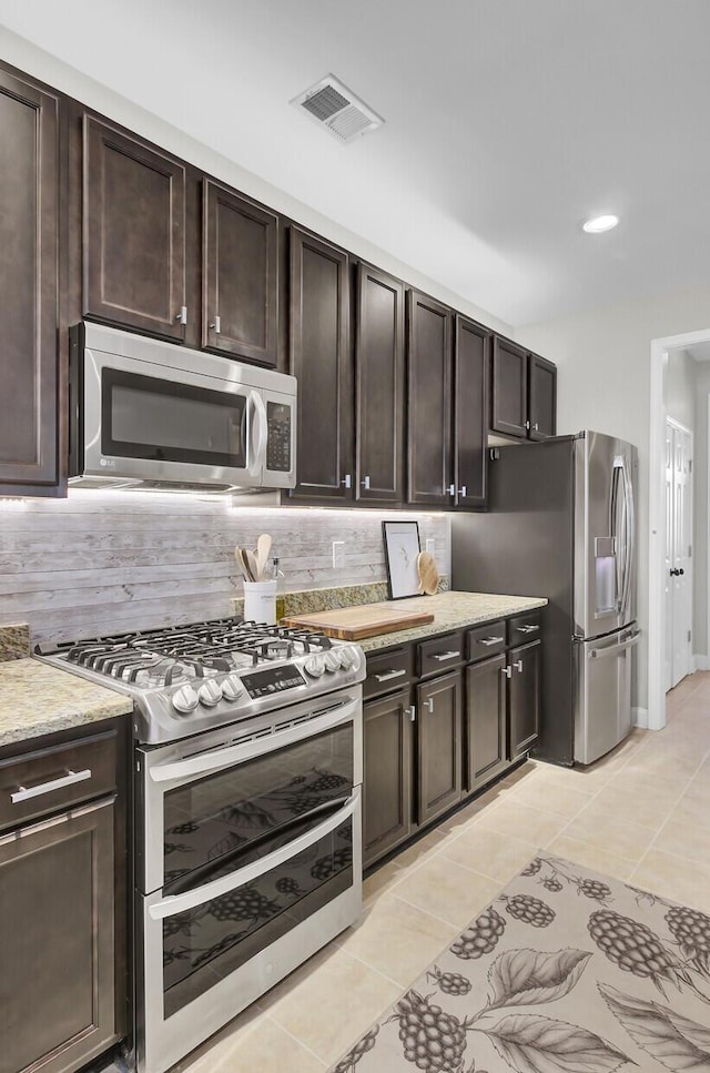 kitchen with dark brown cabinetry, stainless steel appliances, light tile patterned floors, and backsplash