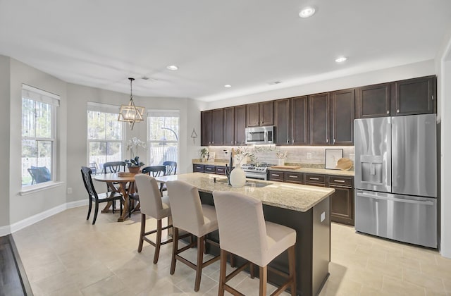 kitchen featuring appliances with stainless steel finishes, decorative light fixtures, sink, light stone counters, and a center island with sink