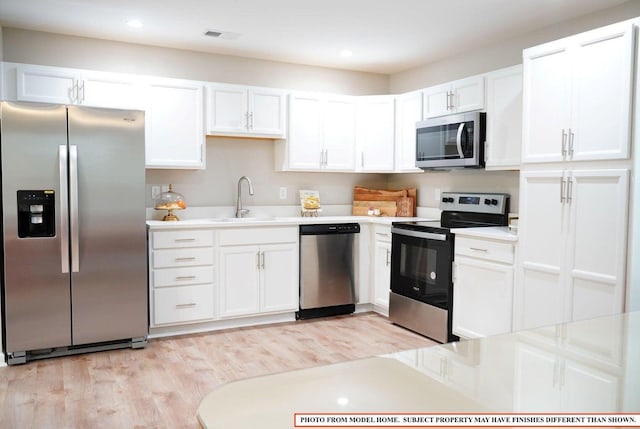 kitchen with appliances with stainless steel finishes, sink, white cabinets, and light hardwood / wood-style flooring