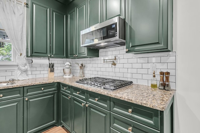 kitchen with green cabinets, stainless steel appliances, and backsplash