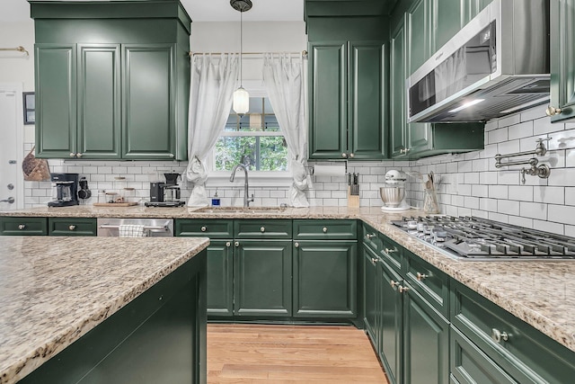 kitchen with green cabinetry, appliances with stainless steel finishes, a sink, and tasteful backsplash