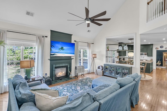 living room featuring a ceiling fan, high vaulted ceiling, a tiled fireplace, and wood finished floors