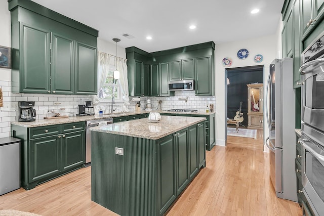 kitchen with green cabinets, stainless steel appliances, a sink, light wood-style floors, and decorative backsplash
