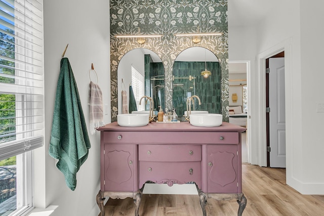 full bath with double vanity, plenty of natural light, wood finished floors, baseboards, and wallpapered walls