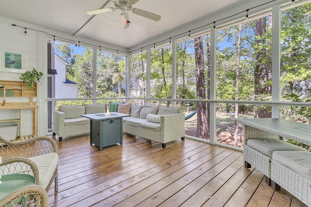 sunroom / solarium featuring an outdoor living space with a fire pit, a ceiling fan, and view of wooded area