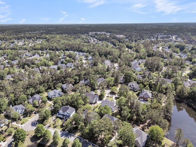 aerial view of property and surrounding area featuring nearby suburban area, a heavily wooded area, and a nearby body of water