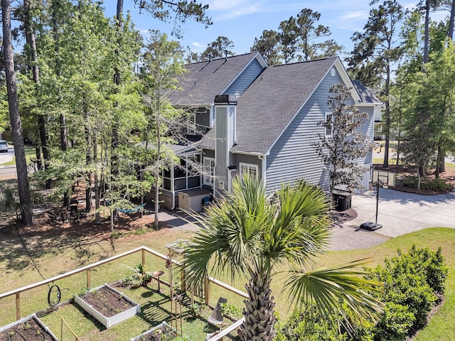 rear view of house with a vegetable garden, a shingled roof, driveway, and fence