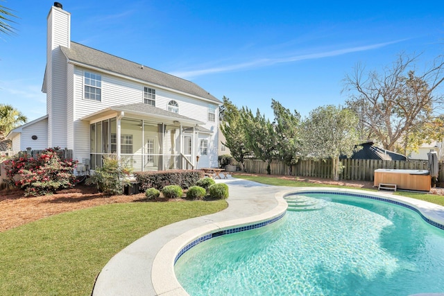 rear view of property with a lawn, a sunroom, and a pool with hot tub