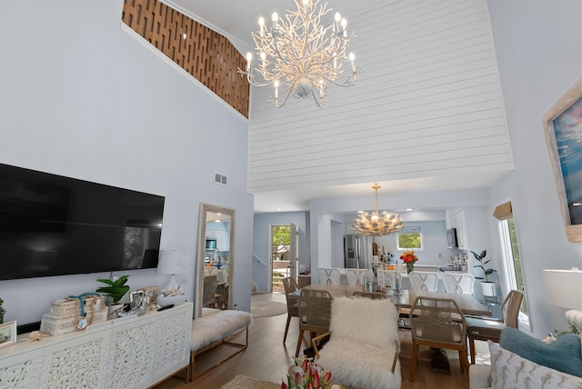 living area with a chandelier, plenty of natural light, a high ceiling, visible vents, and wood finished floors