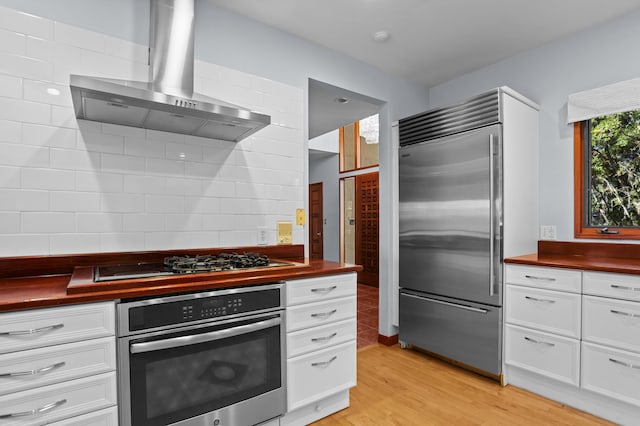 kitchen with white cabinetry, stainless steel appliances, wall chimney range hood, and light wood-type flooring