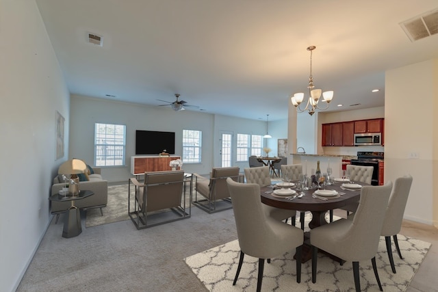 carpeted dining area featuring a healthy amount of sunlight and ceiling fan with notable chandelier