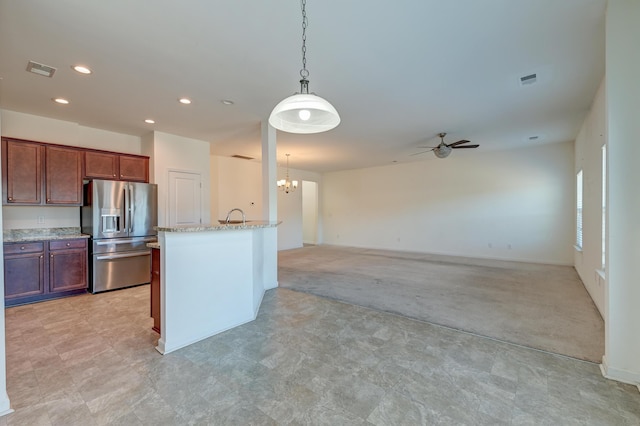 kitchen featuring ceiling fan with notable chandelier, pendant lighting, an island with sink, stainless steel fridge, and light stone countertops