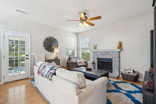 living room with a brick fireplace, a wealth of natural light, ceiling fan, and light hardwood / wood-style flooring