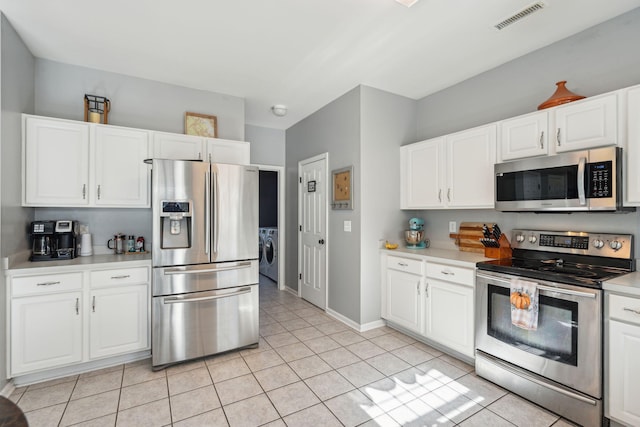 kitchen with light tile patterned flooring, appliances with stainless steel finishes, washing machine and dryer, and white cabinets