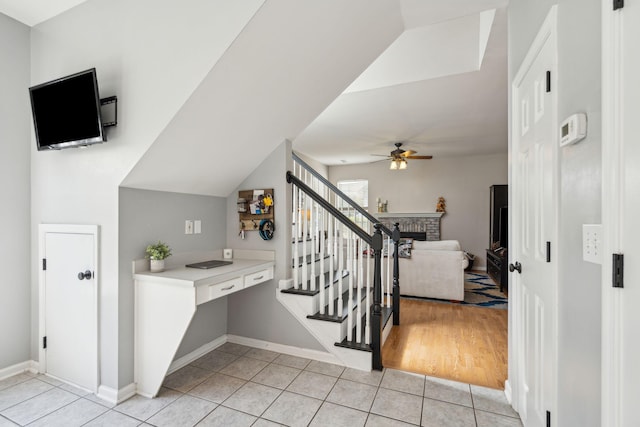 staircase with ceiling fan, tile patterned floors, and a brick fireplace