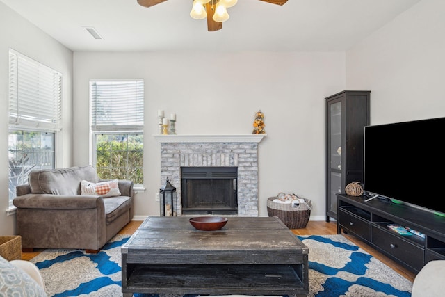 living room featuring ceiling fan, a brick fireplace, and light wood-type flooring