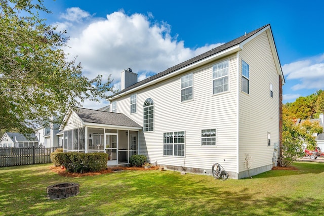 back of house featuring a sunroom, a yard, and a fire pit