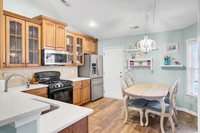 kitchen featuring visible vents, lofted ceiling, stainless steel appliances, light wood-type flooring, and backsplash