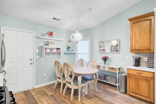 dining space featuring baseboards, light wood-type flooring, visible vents, and a notable chandelier