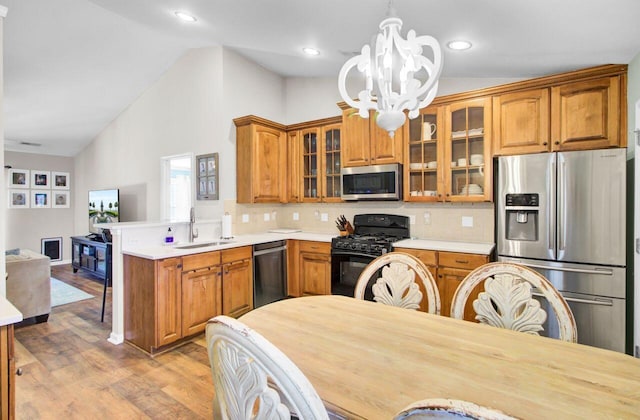 kitchen with a notable chandelier, a peninsula, a sink, appliances with stainless steel finishes, and brown cabinetry