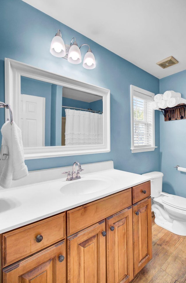 bathroom with toilet, visible vents, wood finished floors, and vanity