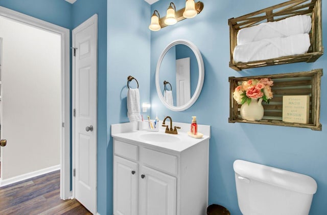 bathroom featuring toilet, baseboards, wood finished floors, and vanity