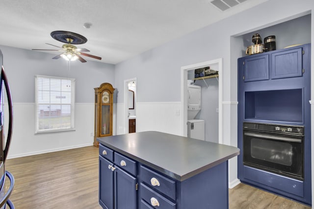 kitchen with a center island, oven, hardwood / wood-style flooring, blue cabinetry, and stacked washer / drying machine