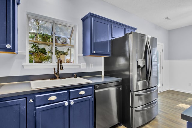 kitchen with a wealth of natural light, sink, blue cabinets, hardwood / wood-style floors, and appliances with stainless steel finishes