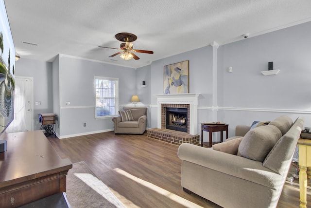 living room with ceiling fan, a brick fireplace, dark hardwood / wood-style floors, a textured ceiling, and ornamental molding