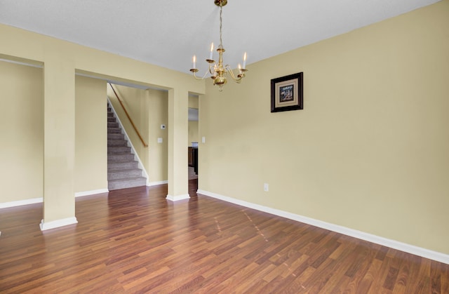 spare room with dark hardwood / wood-style floors and an inviting chandelier